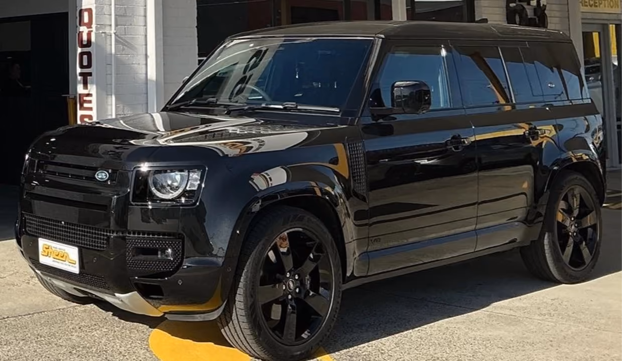 Front-side view of a black Land Rover Defender after repair, with a fully restored front end, clean panels, and a polished finish parked outside a workshop.