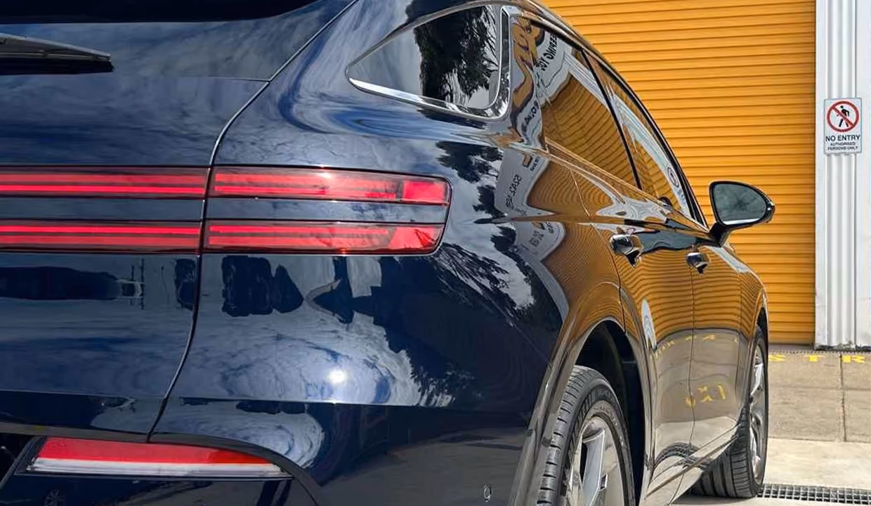 Rear-side view of a dark blue Genesis GV70 after repair, with a smooth, fully restored rear quarter panel and glossy paint finish.