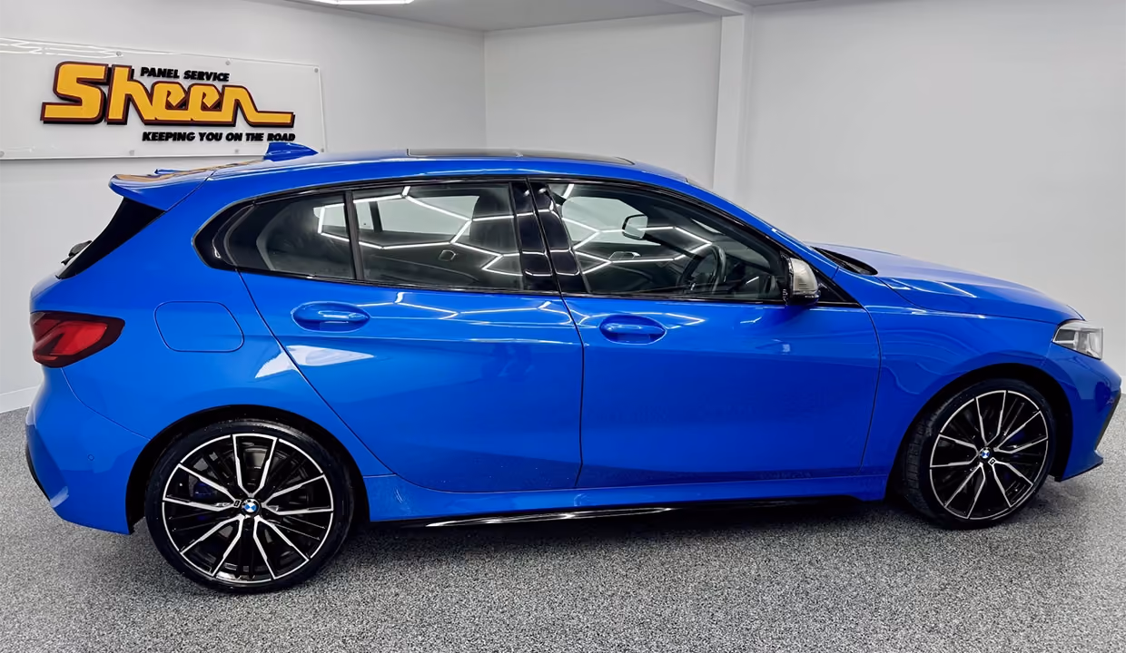 Side view of a blue BMW 1 Series hatchback after repair, with smooth, aligned doors and side panels, restored to a clean, factory-like finish inside a workshop.