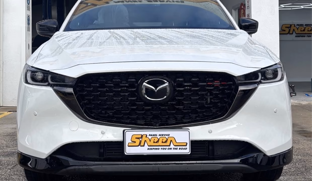 Front view of a white Mazda CX-5 after repair, with a smooth bonnet, aligned grille, and fully restored front end parked outside a workshop.