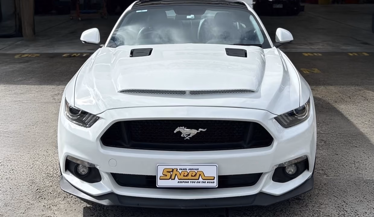 Front view of a white Ford Mustang after repair, with a smooth bonnet, intact grille with emblem, and fully restored front bumper in like-new condition.