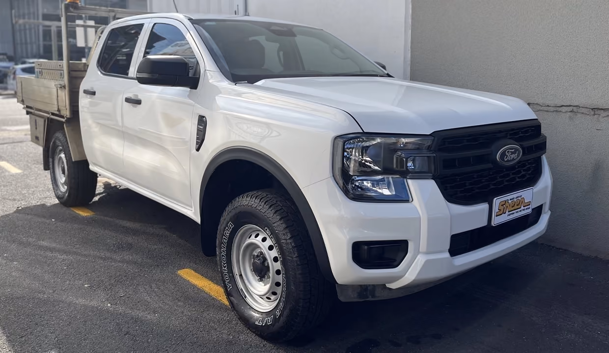 Front-side view of a white Ford Ranger work ute after repair, with a restored front end, aligned panels, and clean finish parked outside a workshop.