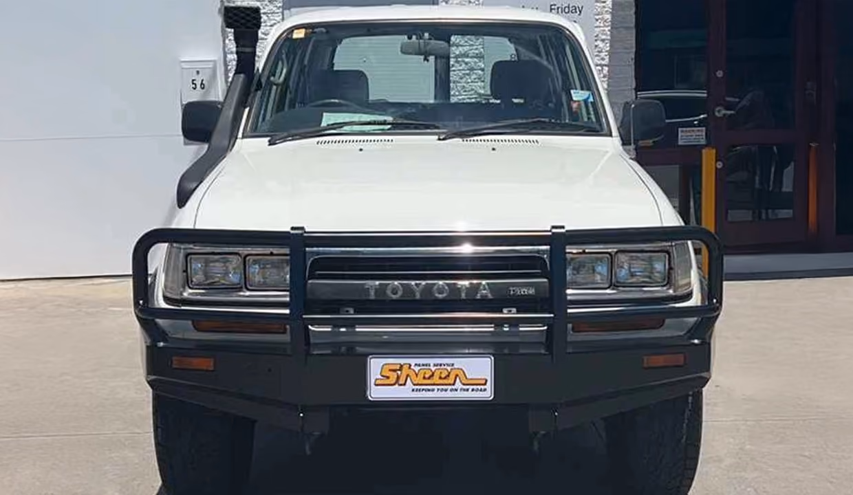 Front view of a white Toyota LandCruiser after repair, with a straight bull bar, aligned grille, and fully restored front end in clean condition.