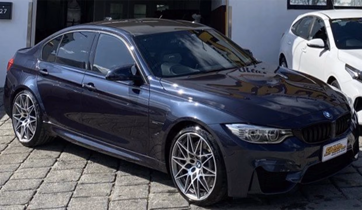 Front-side view of a dark blue BMW M3 after repair, with smooth, aligned body panels and a high-gloss, fully restored finish inside a workshop.