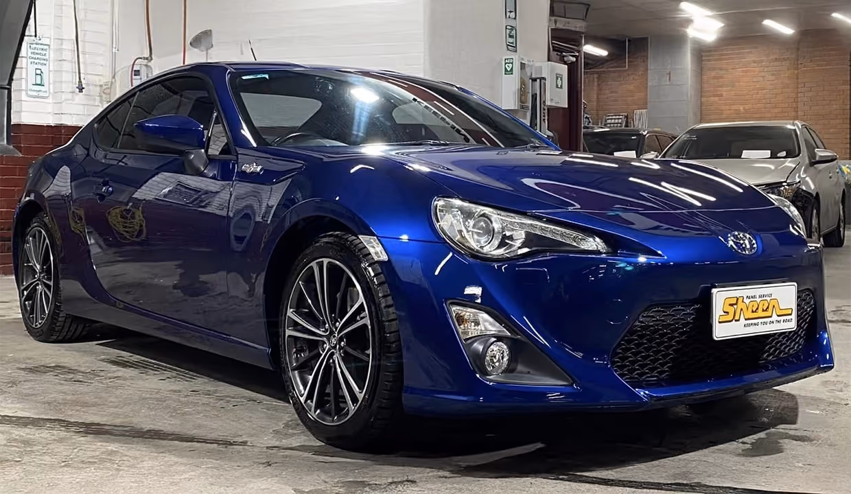 Front three-quarter view of a blue Toyota GR86 after repair, showing a fully restored front end with smooth panels, aligned bumper, and a glossy factory-quality finish.
