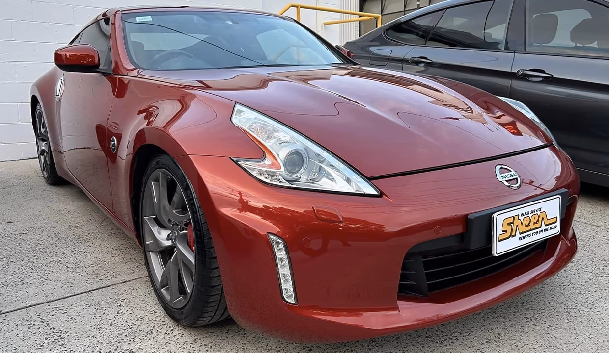Front three-quarter view of a red Nissan Z after repair, featuring a smooth, fully restored side panel and wheel arch with a flawless, high-gloss paint finish.