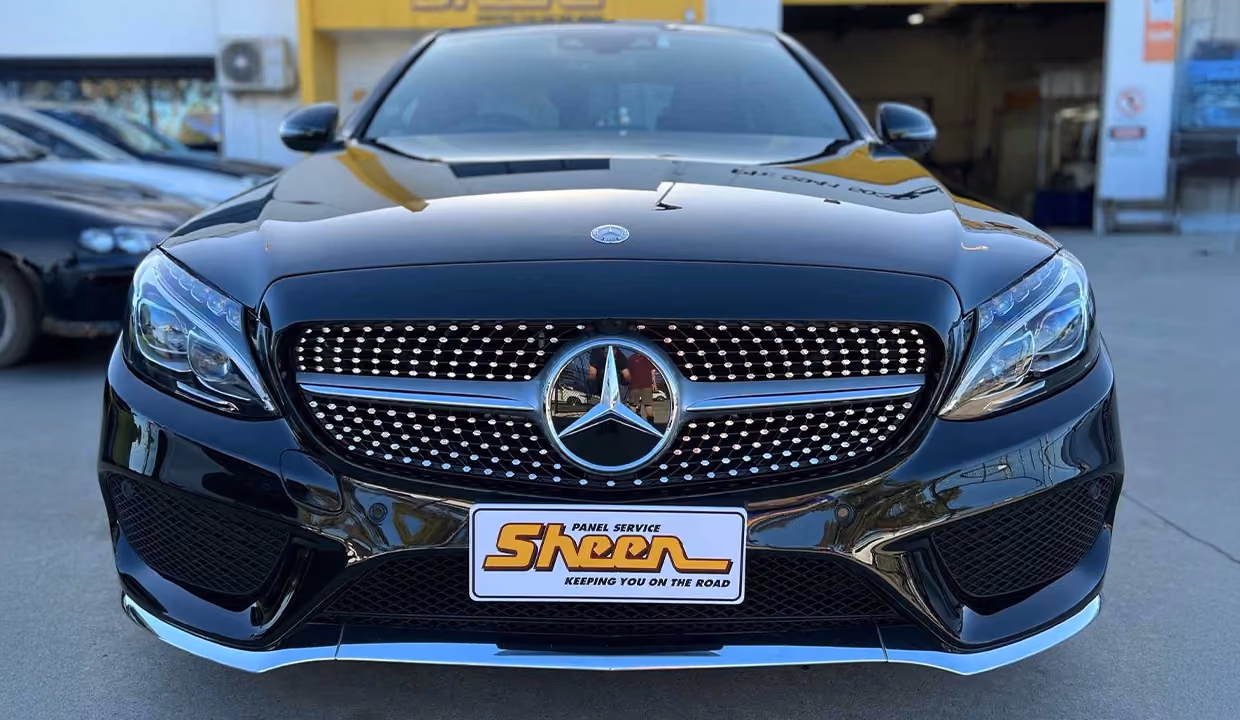 Front view of a black Mercedes-Benz C-Class after repair, featuring a perfectly aligned grille, restored bumper, and a flawless, high-gloss finish with factory-quality detail.