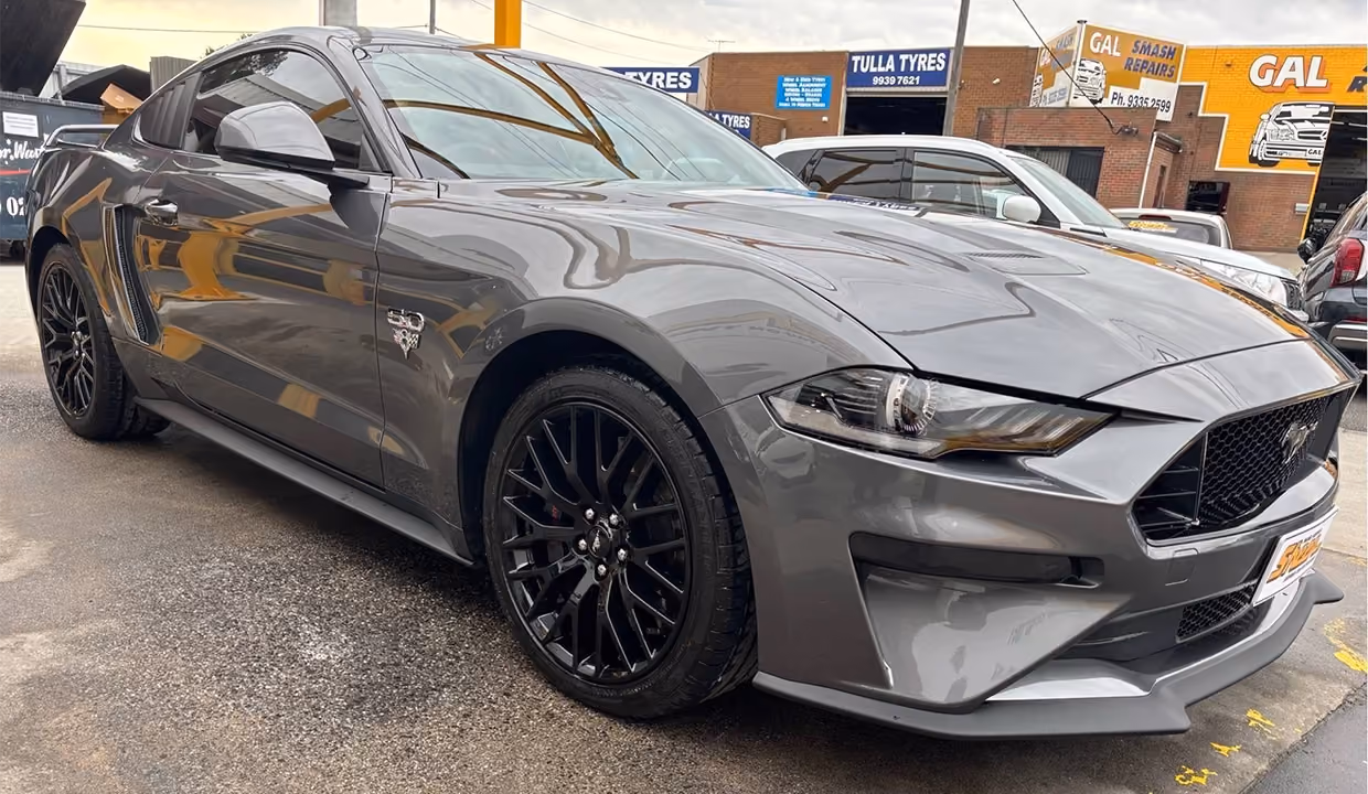 Front-side view of a Ford Mustang after front-end repair, featuring a fully restored quarter panel and headlight area with smooth paintwork and a flawless finish.