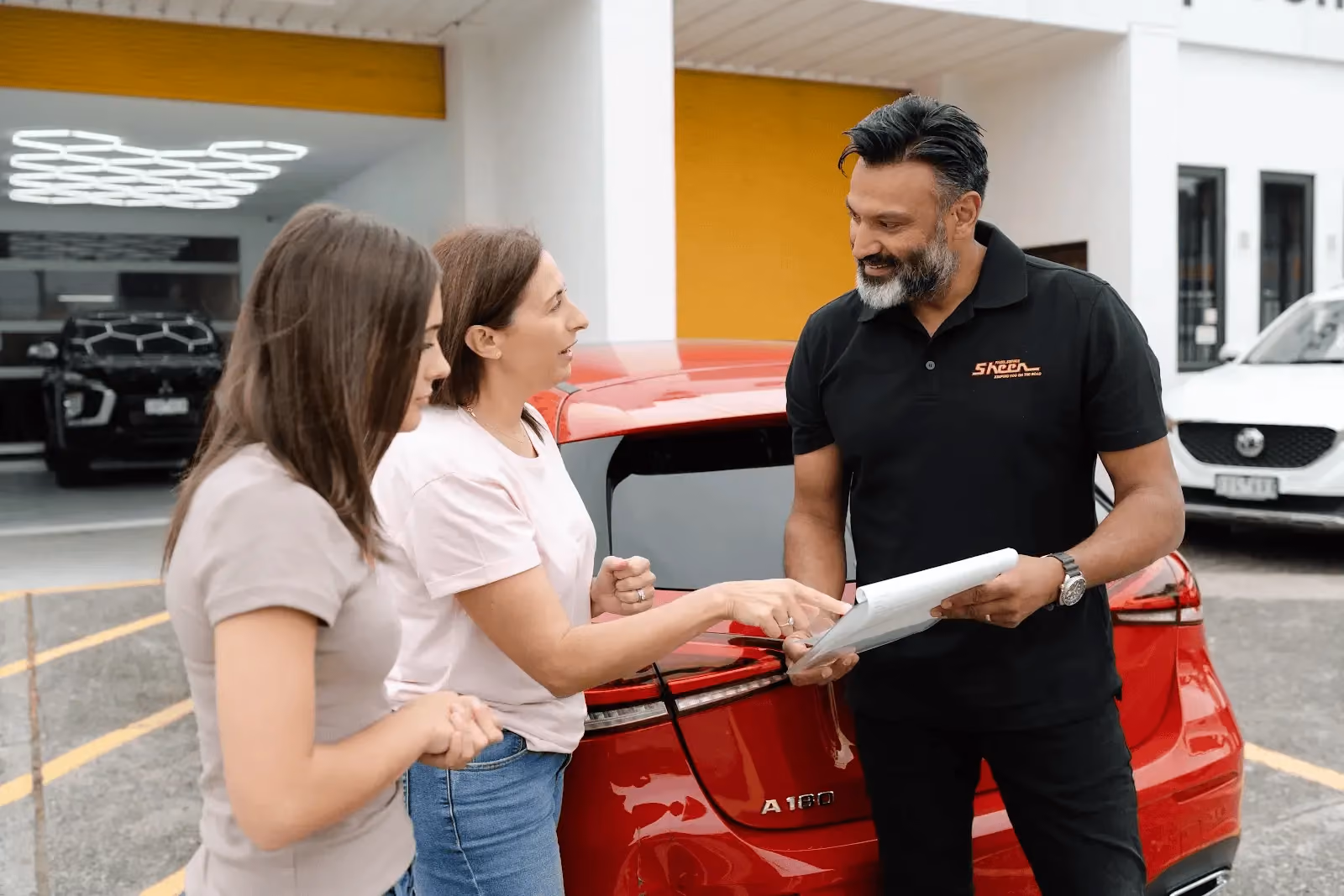 Customer reviewing paperwork with a Sheen representative beside a vehicle.]