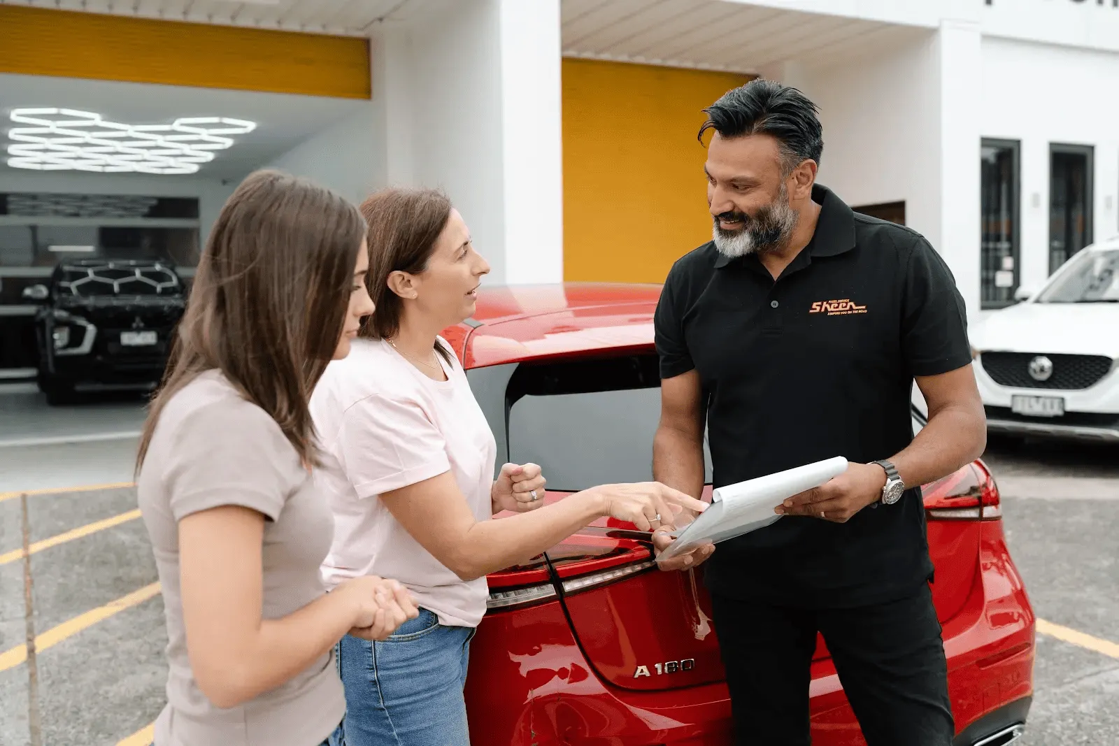 Customer reviewing paperwork with a Sheen representative beside a vehicle.]