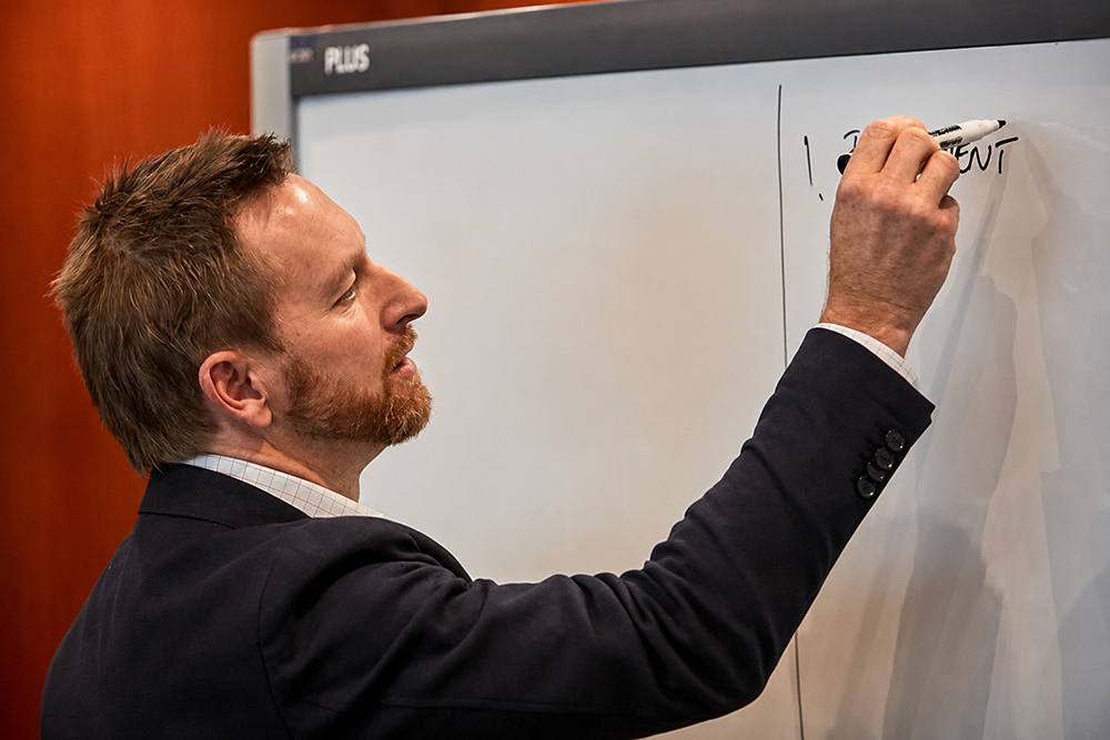 Jason Trewin writing on a whiteboard during a technical training session.