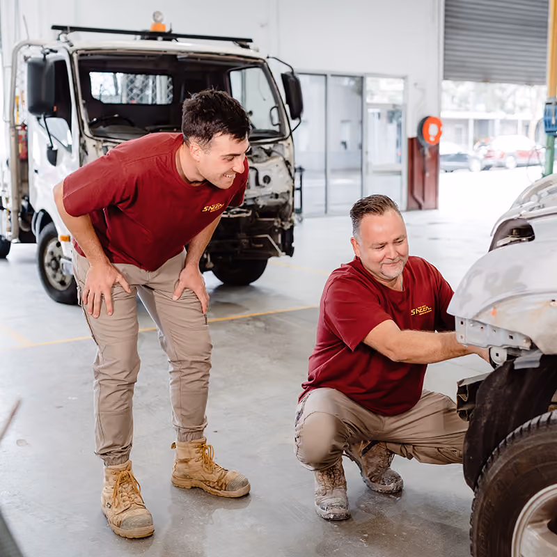 Two Sheen technicians inspecting bodywork on a vehicle in the workshop.