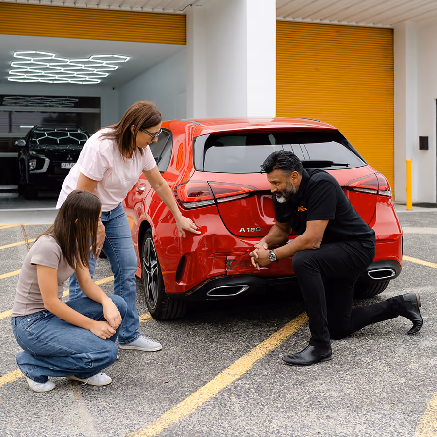 Sheen specialist inspecting rear car damage with two customers outside a workshop