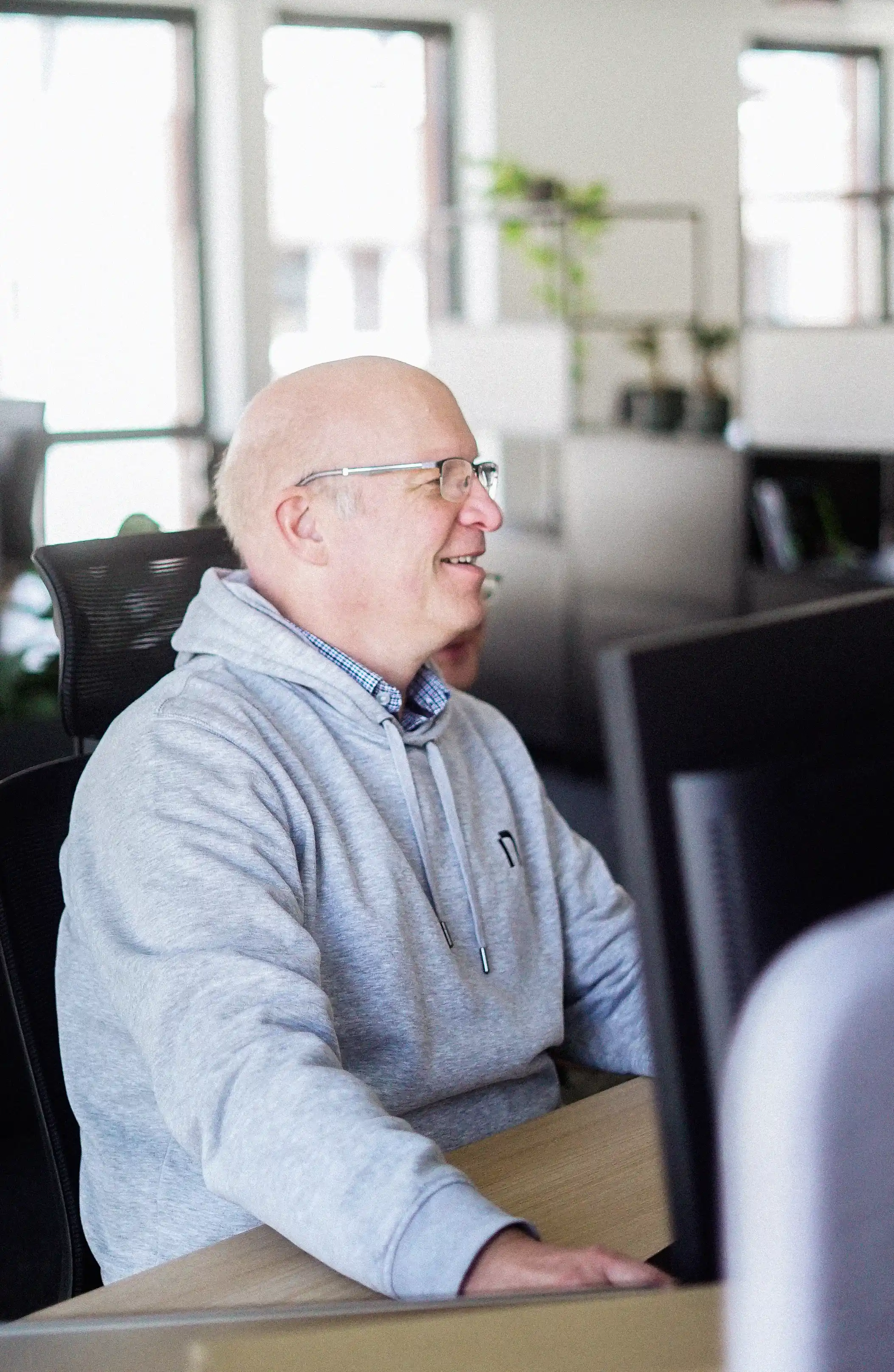 A man sitting in front of an desktop, working and laughing.