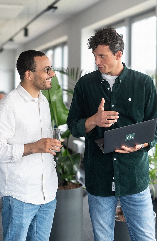 Two men standing and talking with each other. Holding a Laptop.
