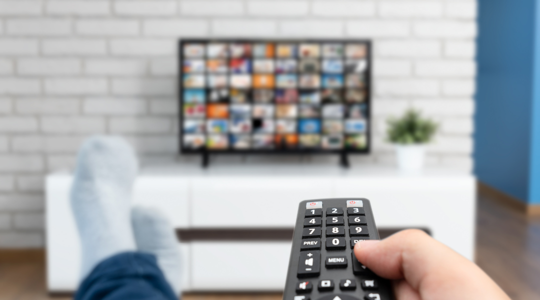 A person point a remote at a TV with multiple streaming service apps on it