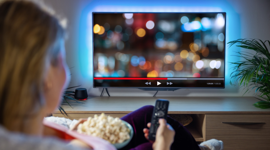 A blonde woman watching TV holding popcorn on the sofa
