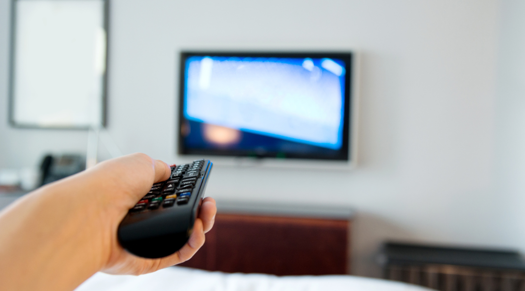 A woman pointing a TV remote at a mounted TV screen