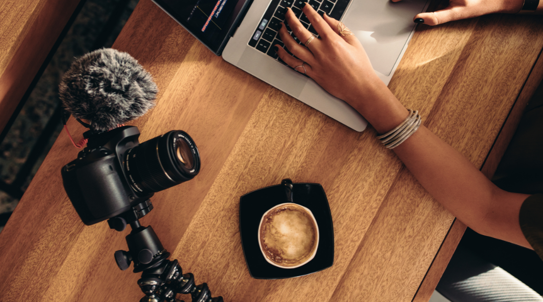 A camera on a tripod with a mic next to a woman editing on a mac book