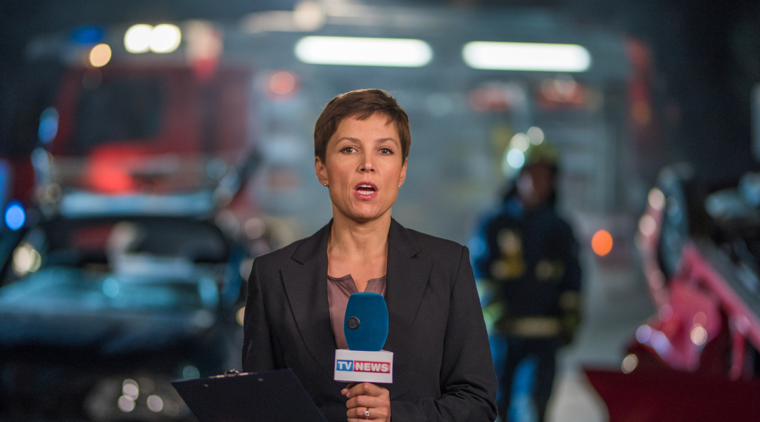 A woman news reporter standing in front of a car crash