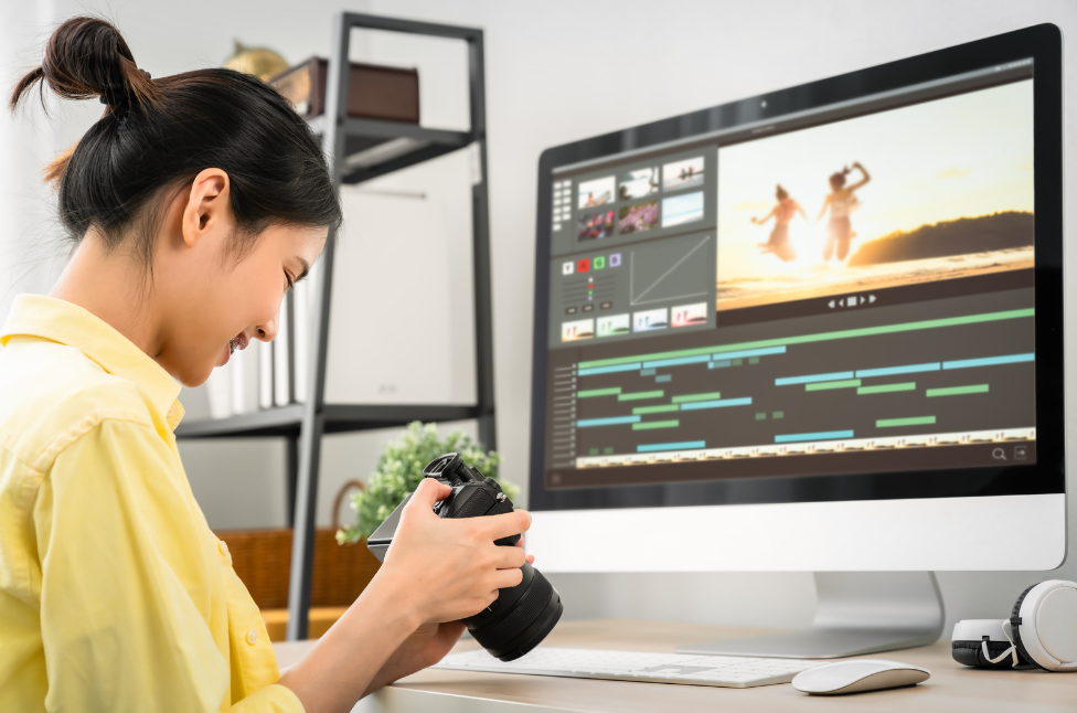 A woman holding a camera checking what's on the screen. She is sitting in front of her desk. On the desk, a video editing screen is turned on.