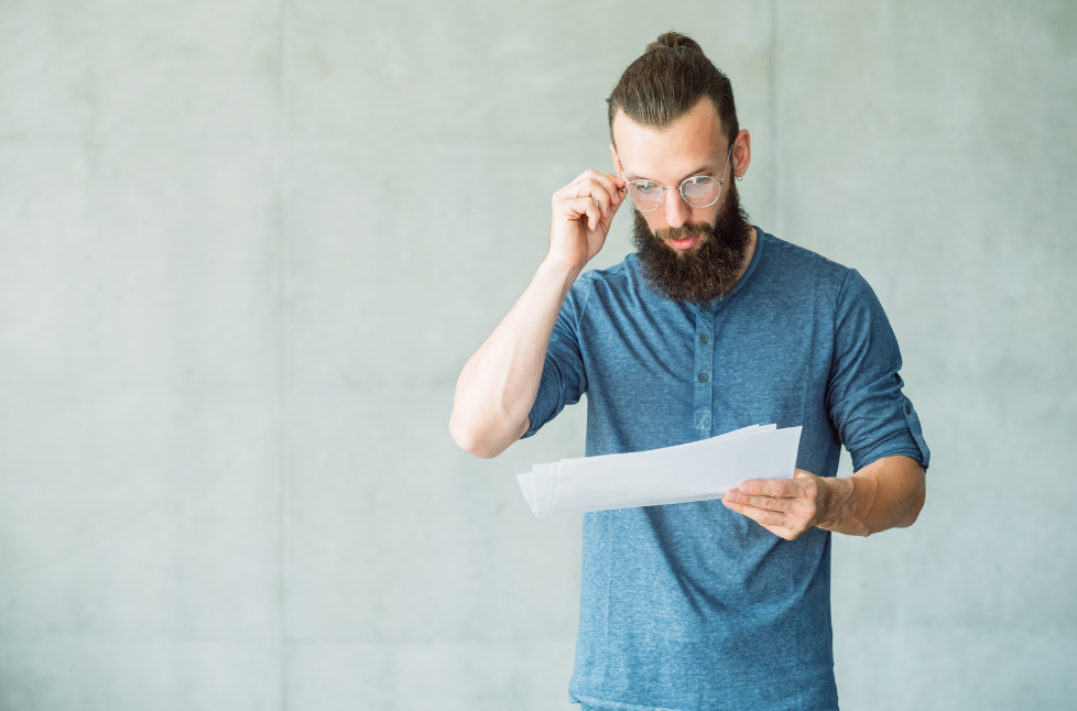 A man looking at some paper. He is adjusting his glasses with his right hand.