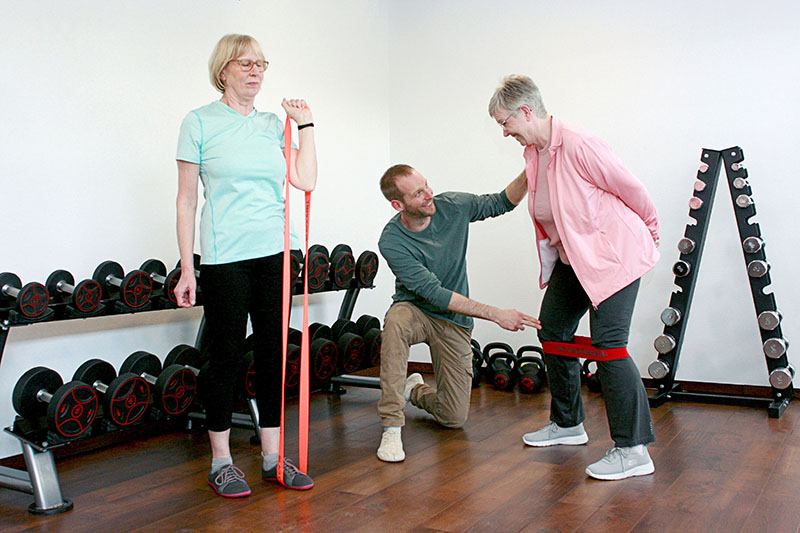 Physiotherapeut zeigt Patienten Übungen mit Terra-Band