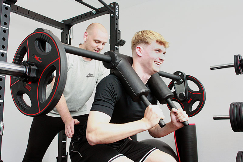 Physiotherapeut macht Kraftübunge Squats am Gerät mit Patient