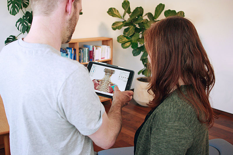 Physiotherapeut zeigt Patientin Skizze eines Skeletts auf dem iPad