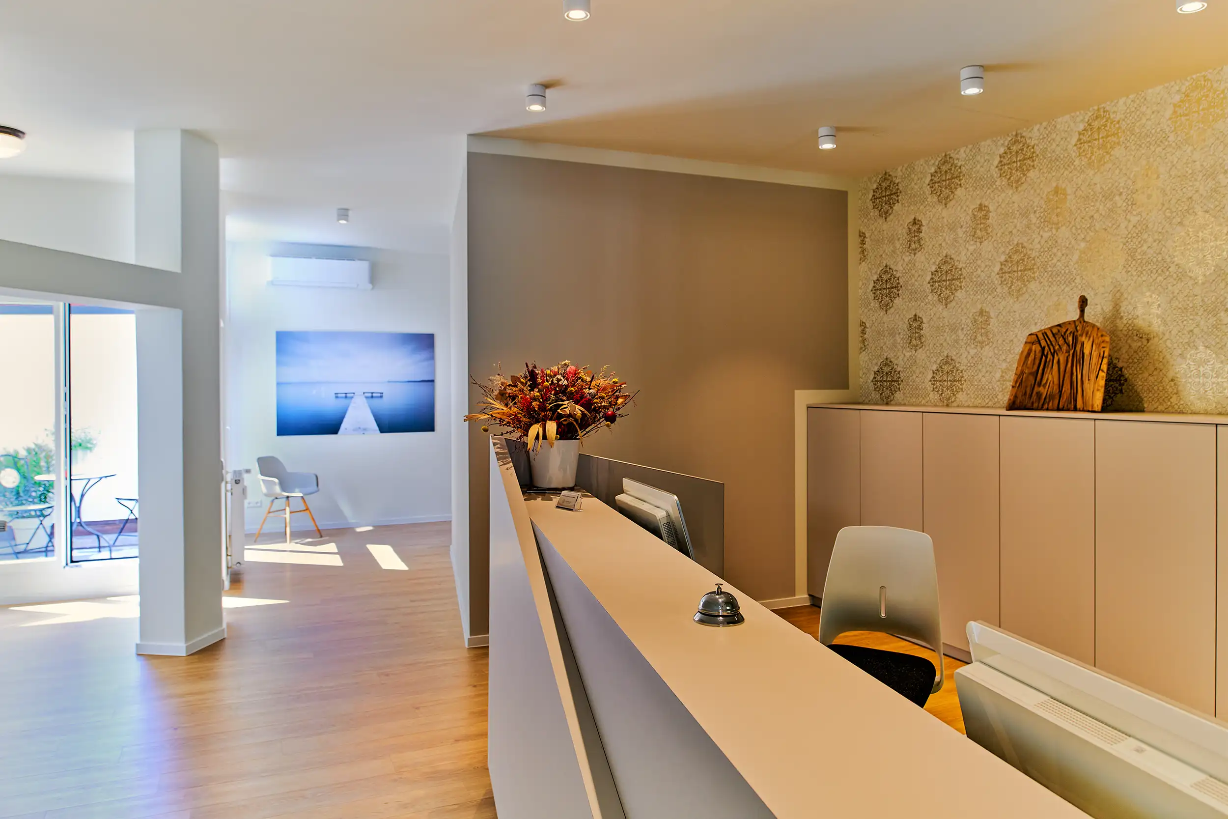 Moderne Rezeption mit Blumendeko, Stuhl und gemütlichem Wartebereich mit Kunstbild im Hintergrund.