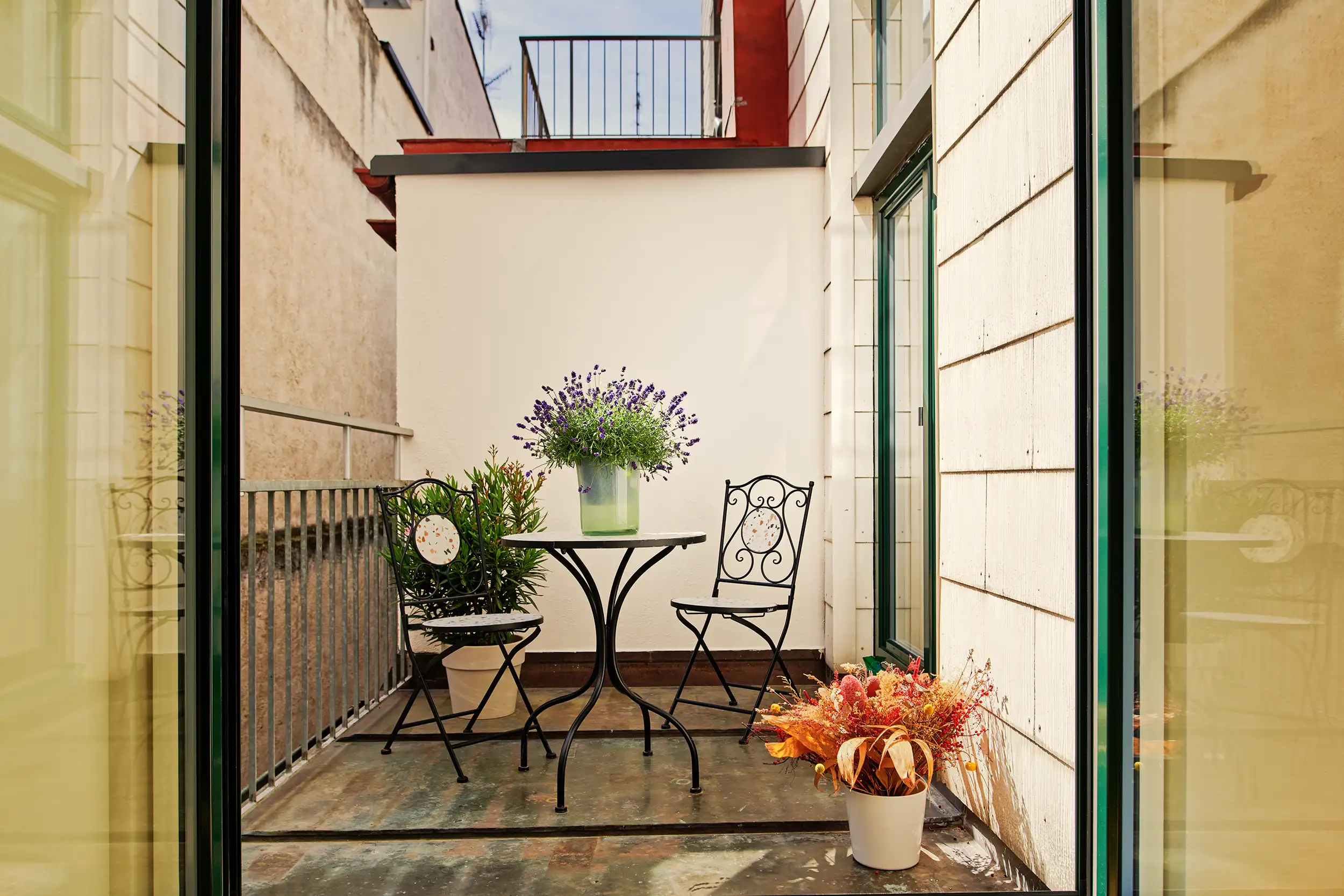 Open-Air Terrasse mit rundem Tisch, zwei Stühlen und Blumen in Töpfen bei Sonnenschein, Aufenthalt für Patient*innen