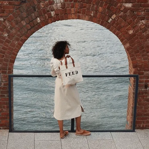 Woman standing next to the water with a shopping bag.