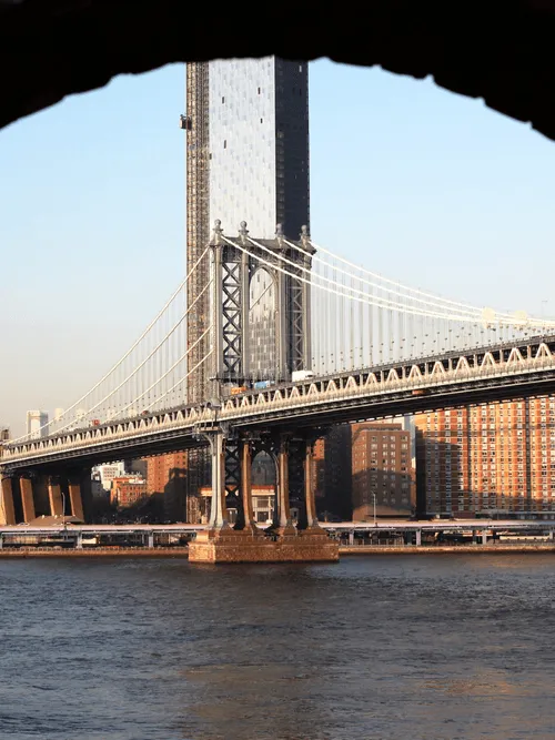 Image of the New York City skyline behind a suspension bridge.