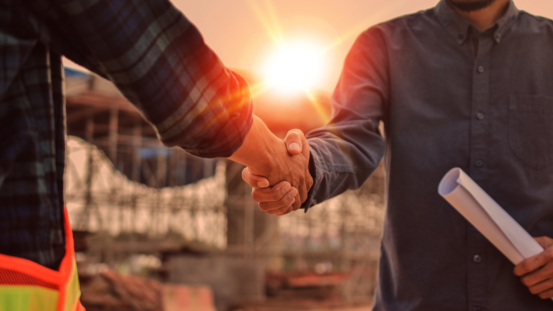 General contractor and construction CFO shaking hands on a jobsite at sunset.