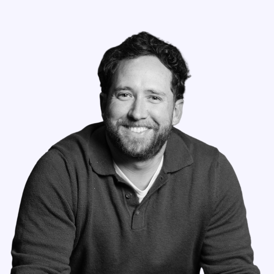 A black and white headshot of Caleb Lush smiling on a light purple background