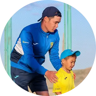 Man in blue sportswear guiding a young boy in yellow sportswear outdoors.