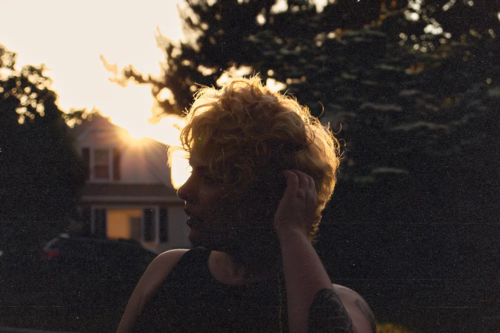 Twilight portrait of Jill facing portrait in front of a house with the sunset peeking out behind the roof