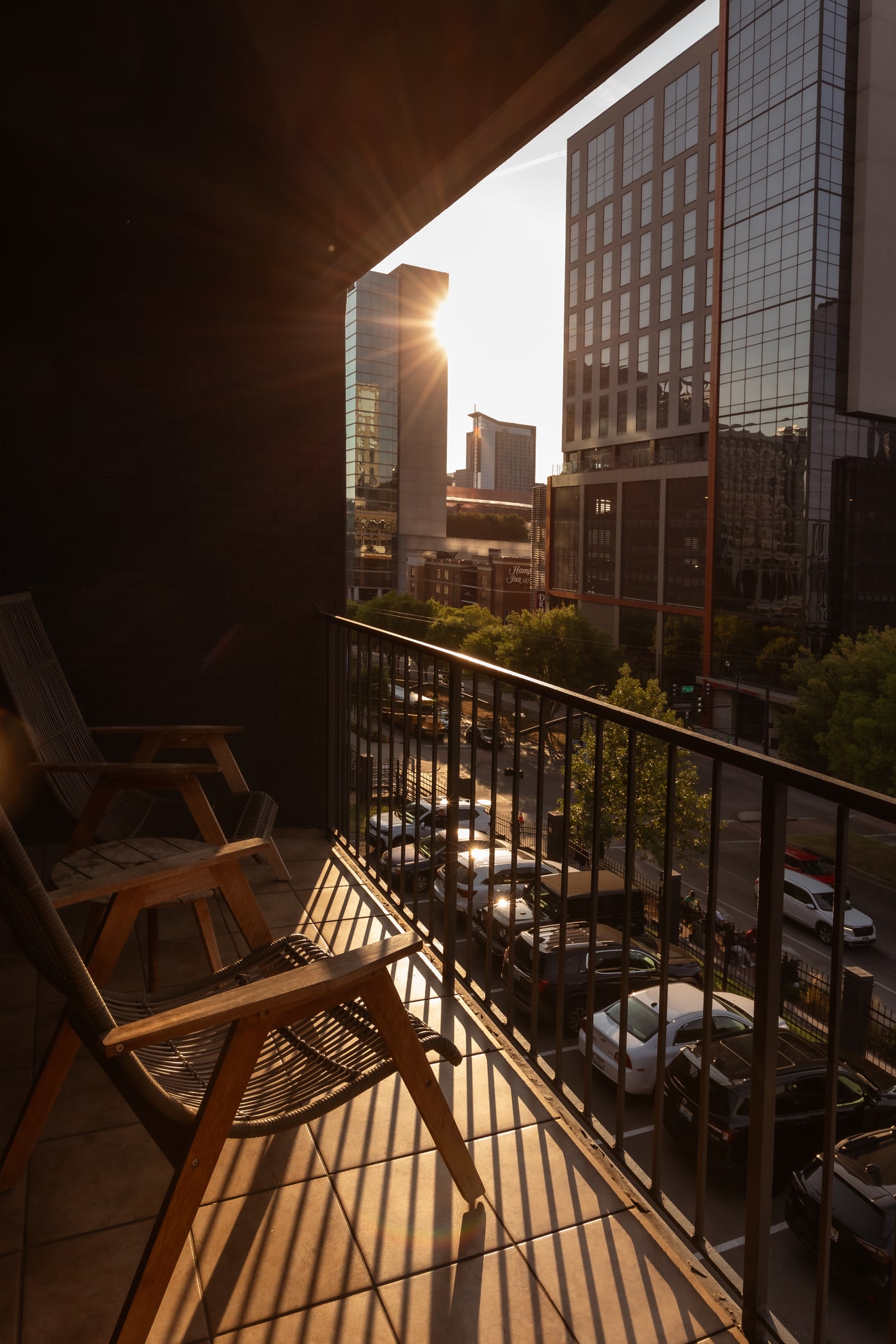 Balcony with lounge chairs overlooking modern city skyline at sunset, warm golden light and long shadows.