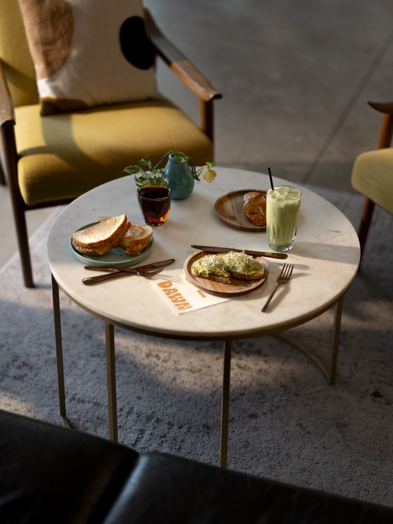 Breakfast and coffee on round lounge table at DAWN, toast, pastry, espresso and iced matcha latte.