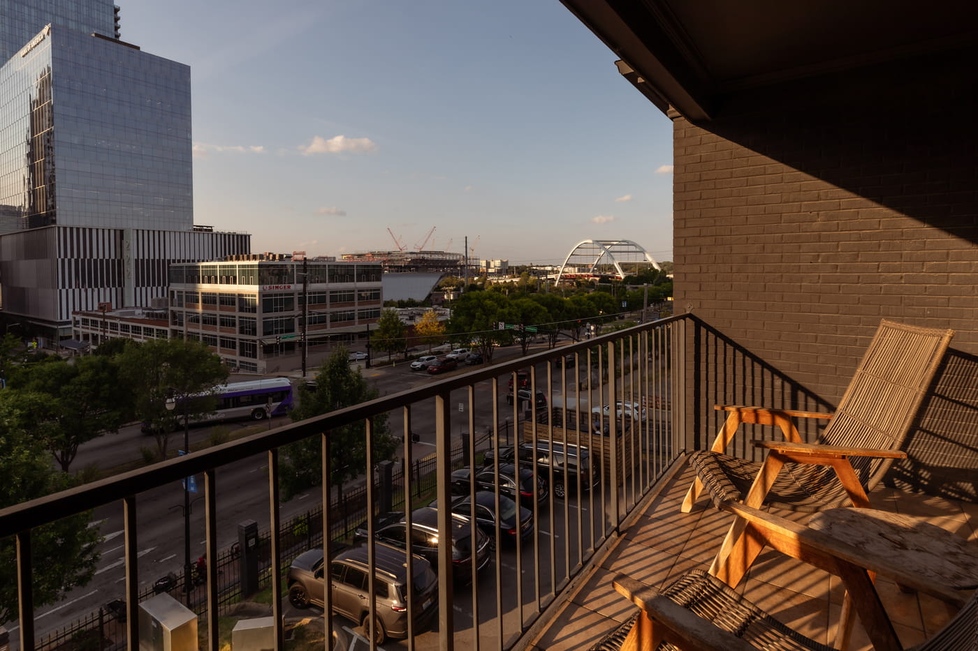 Urban balcony view with woven lounge chairs overlooking downtown cityscape, parking lot, and arched bridge at golden hour