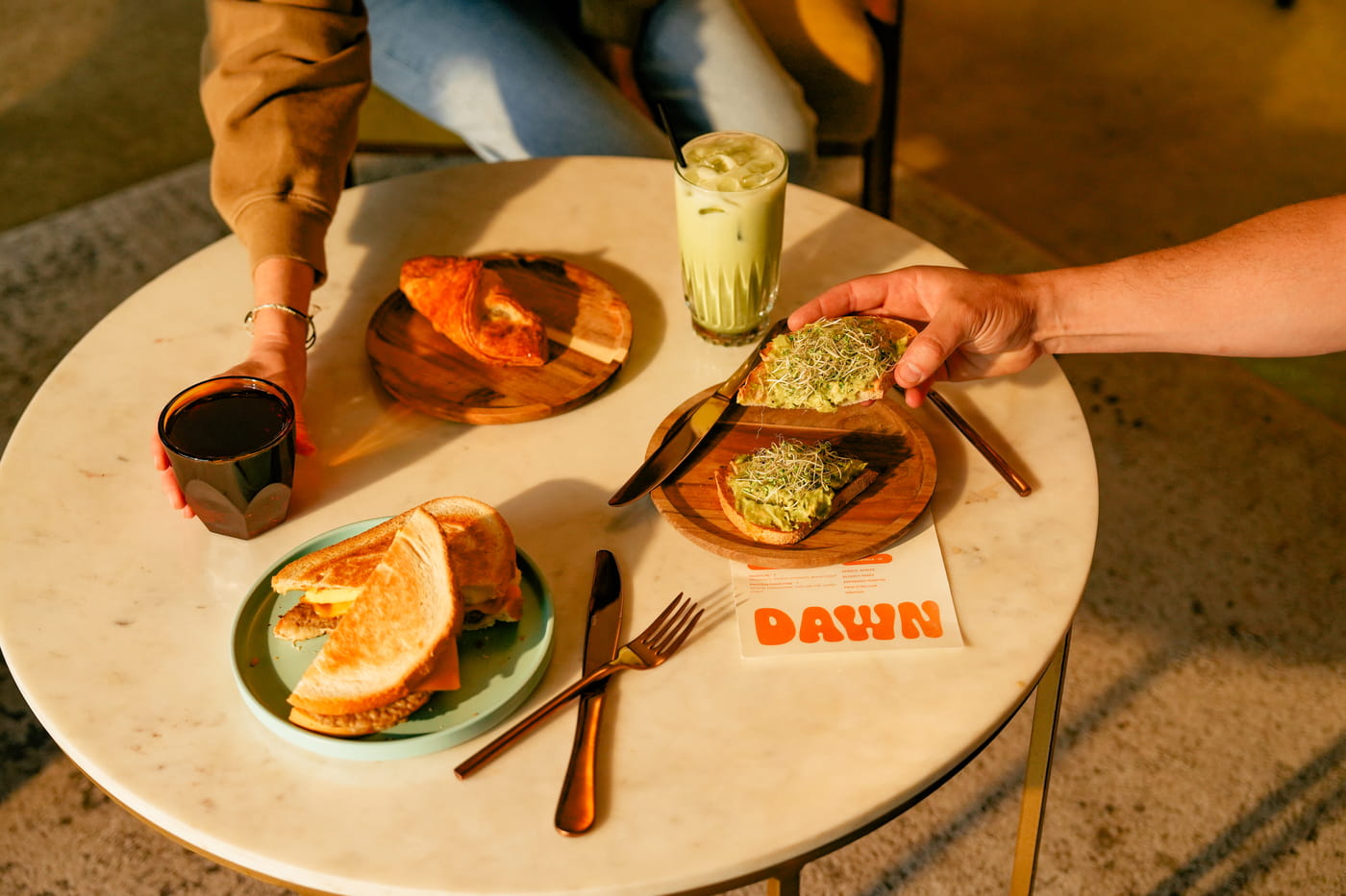 Brunch spread at Dawn cafe featuring avocado toast with sprouts, croissant, grilled sandwich, iced matcha latte and coffee