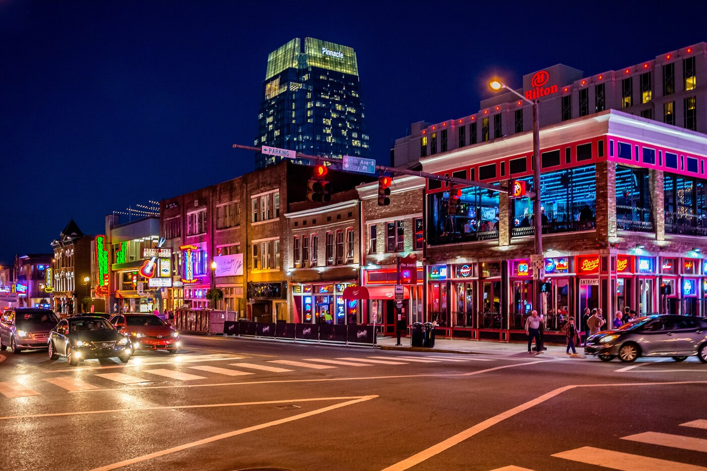 Nashville Broadway street at night with neon-lit honky tonks, live music venues, Pinnacle tower and Hilton hotel in