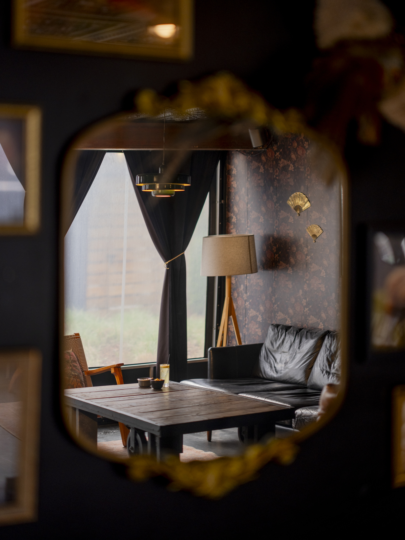 Cozy vintage cafe interior reflected in ornate gold mirror featuring leather sofa, wooden table, and floral wallpaper