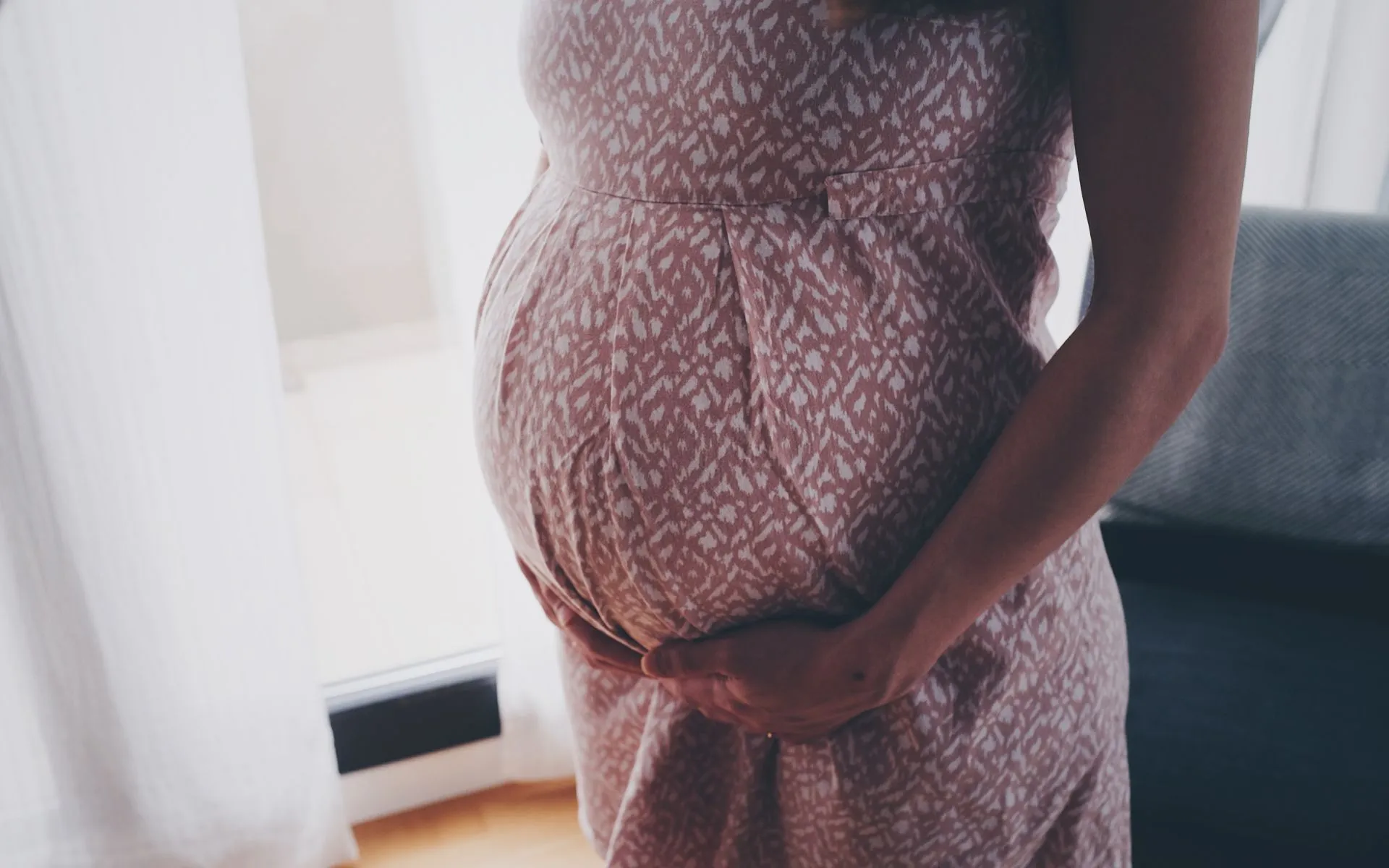 A mother stands near the mirror in her bedroom, holding her bump. 