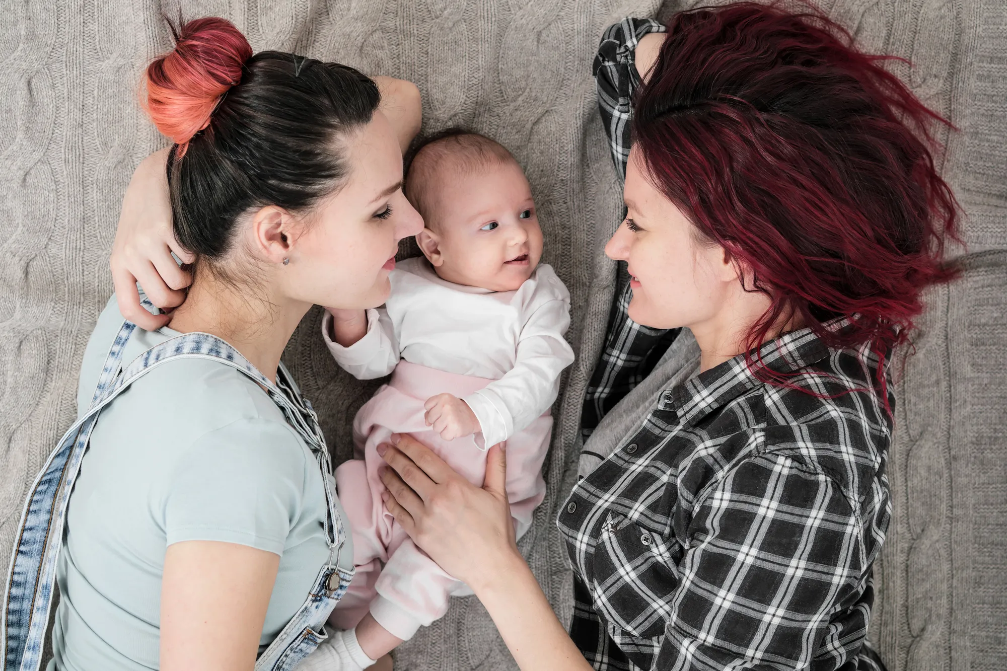 parents kiss their newborn while laying on a bed together