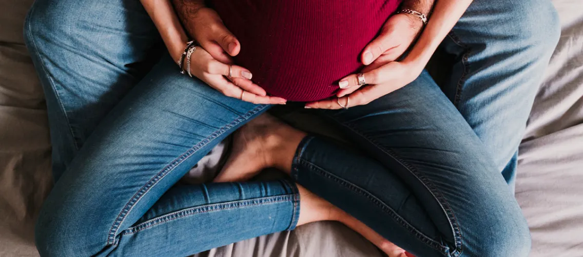 A pregnant woman comfortably seated on her husband's lap, illustrating support.