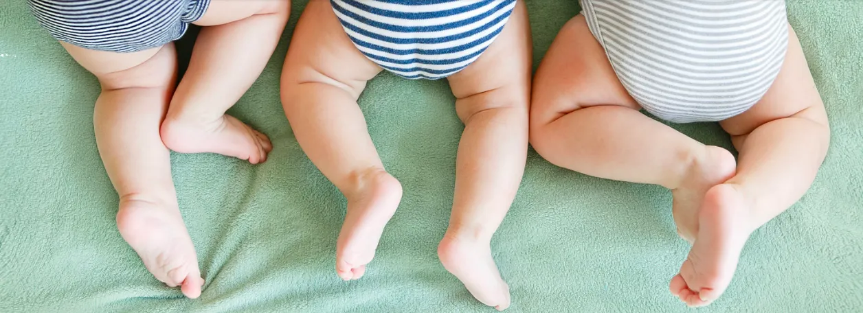 Three babies in diapers are lying on a green blanket, smiling and playing together in a cozy setting.