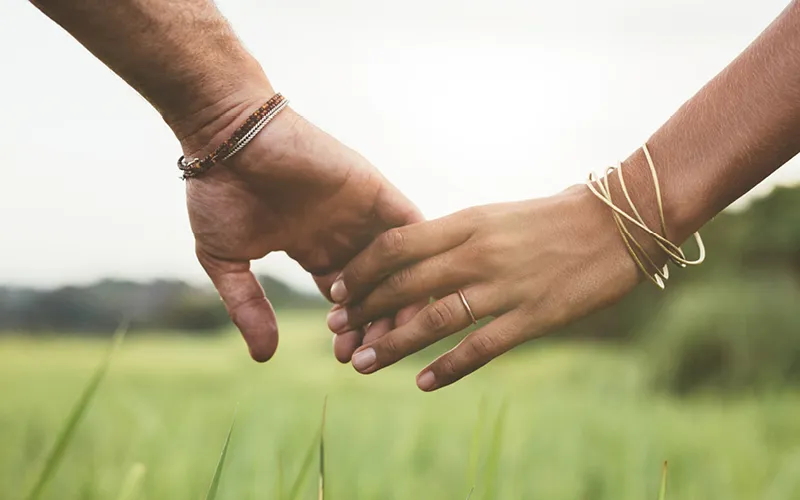 A couple holds hands as the walk through a green field.