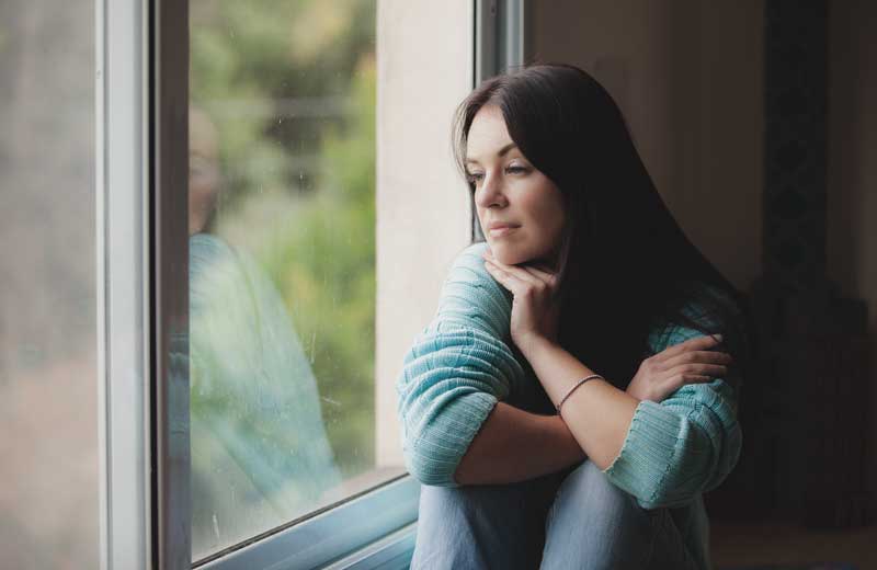 Woman sits at window looking out.