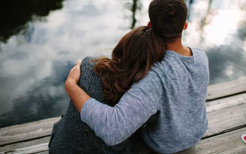 Image of parents sitting by a lake, embracing. 